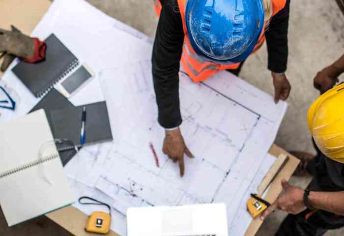Two workers in hardhats viewing construction blue prints from above.